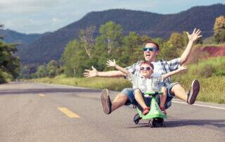 Father and son having fun riding a scooter down the road