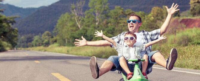 Father and son having fun riding a scooter down the road